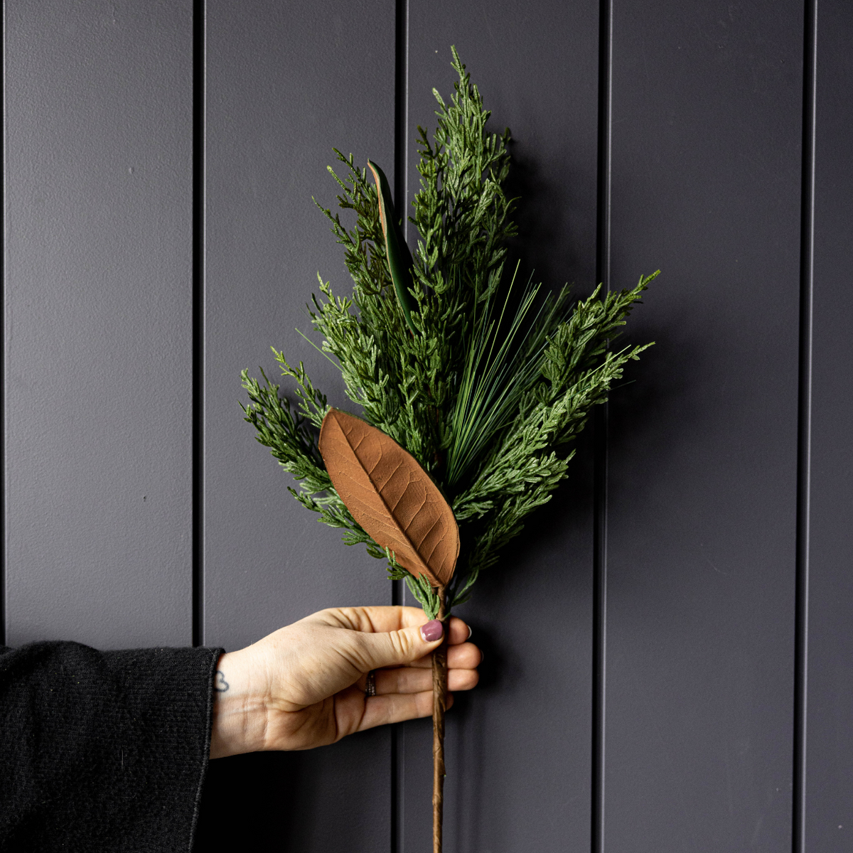 Hand holding a small bouquet of greenery against a dark wooden panel background